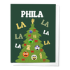 A Christmas-themed greeting card with a green background featuring a Christmas tree and various cartoon characters from Philly sports. The text 'PHILA LA LA' is prominently displayed.