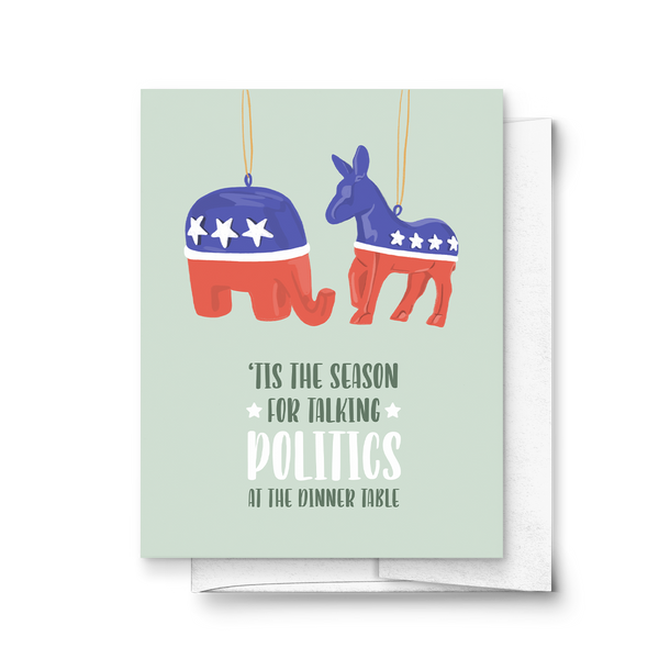 A greeting card with a humorous illustration of a democrat and republican Christmas ornaments, with the text 'Tis the season for talking POLITICS at the dinner table'. The card is set against a light green background.