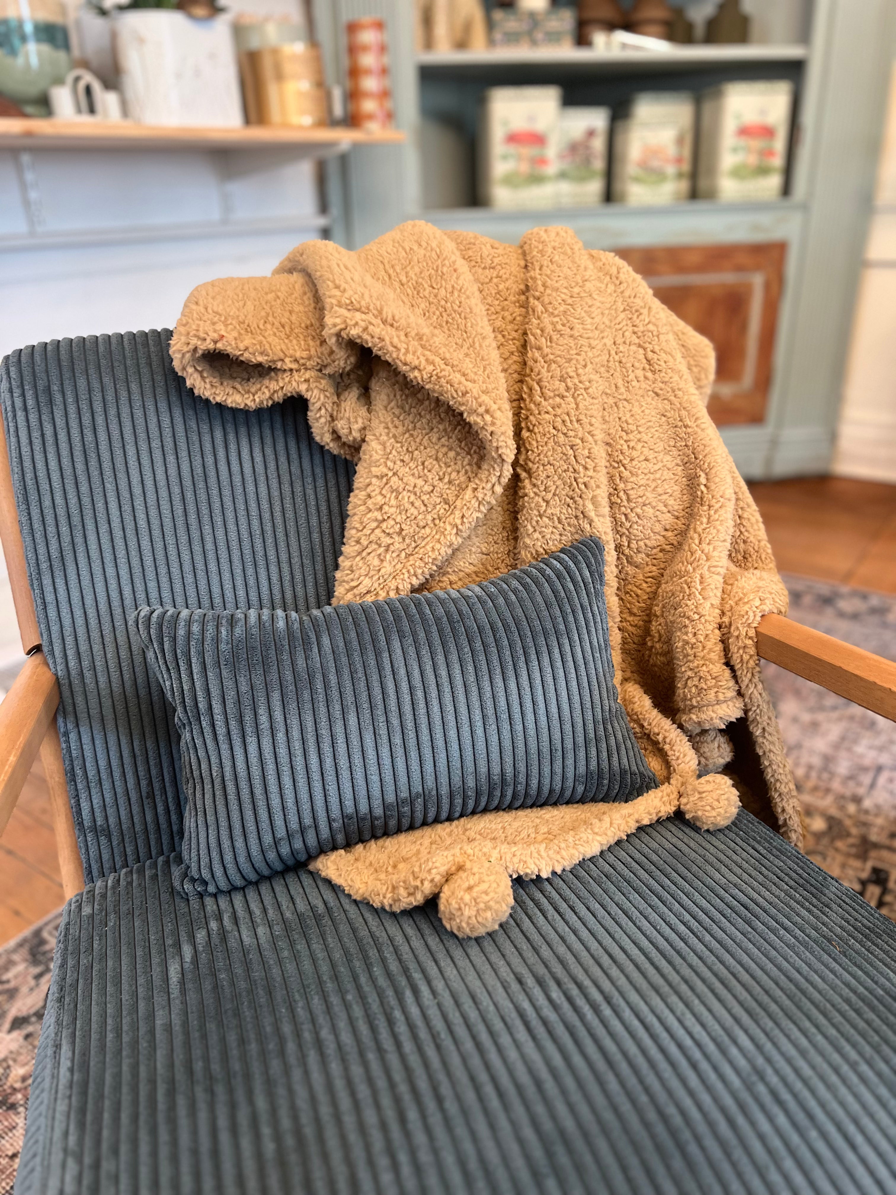 Gray cushion on a chair with a beige blanket draped over it in a cozy room.