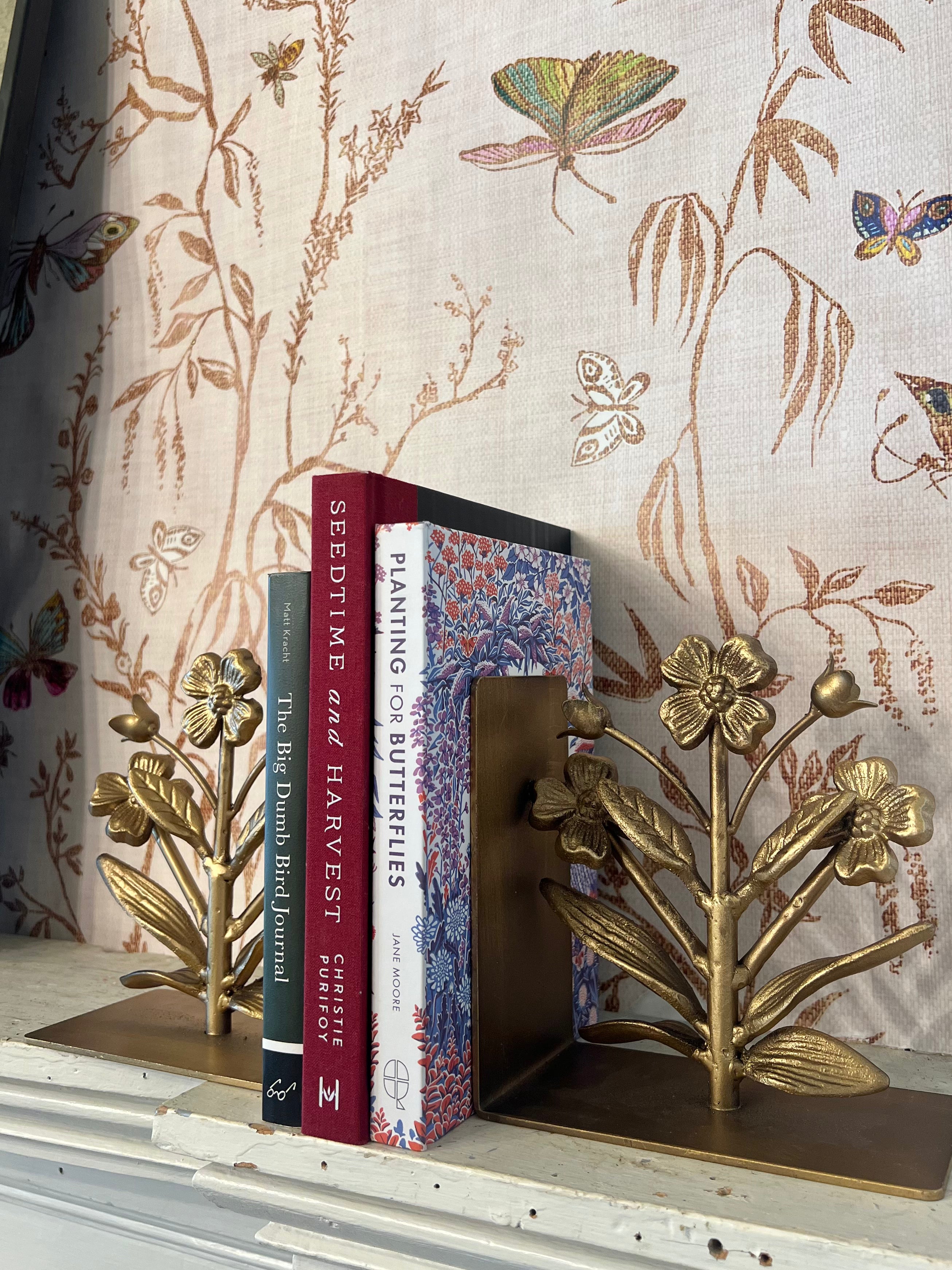 Gold floral bookends holding books against a decorative wallpaper background