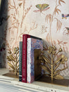 Gold floral bookends holding books against a decorative wallpaper background