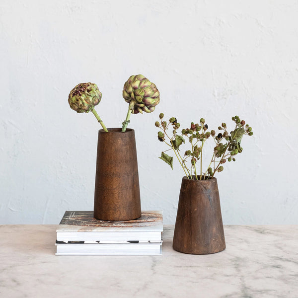 Two rustic wooden vases with plants on a light surface and white background
