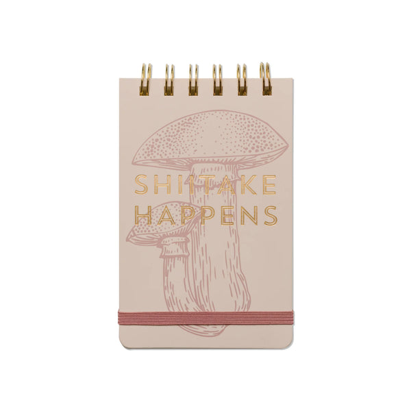 Notebook with mushroom illustration and 'Shitake Happens' text on a beige background
