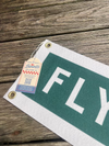 Fabric banner with 'FLY' text on a wooden surface, featuring a brand tag.