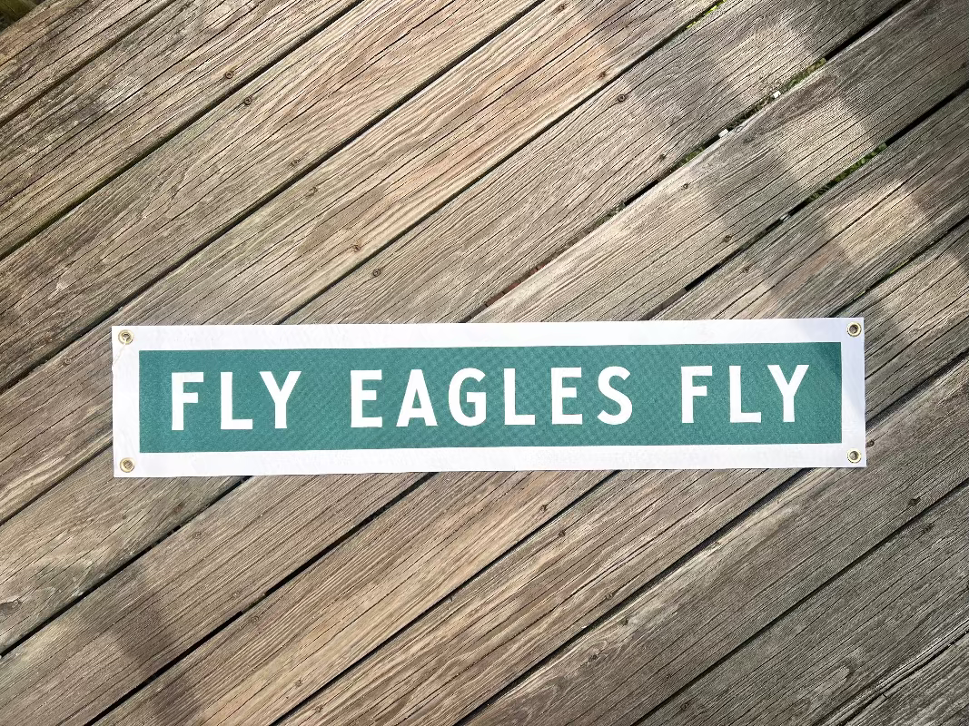 Street sign with 'Fly Eagles Fly' on a wooden surface