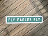 Street sign with 'Fly Eagles Fly' on a wooden surface