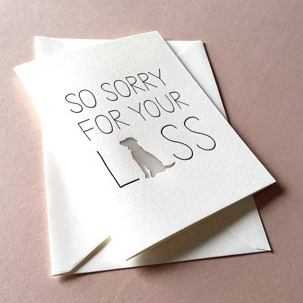 A folded sympathy card with 'SO SORRY FOR YOUR LOSS' printed in black on a white background, featuring a small illustration of a dog. The card is presented with a coordinating envelope.
