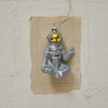 A hand-painted glass astronaut ornament with a peace sign and glitter, featuring a silver and gold finish, displayed on a textured wall.