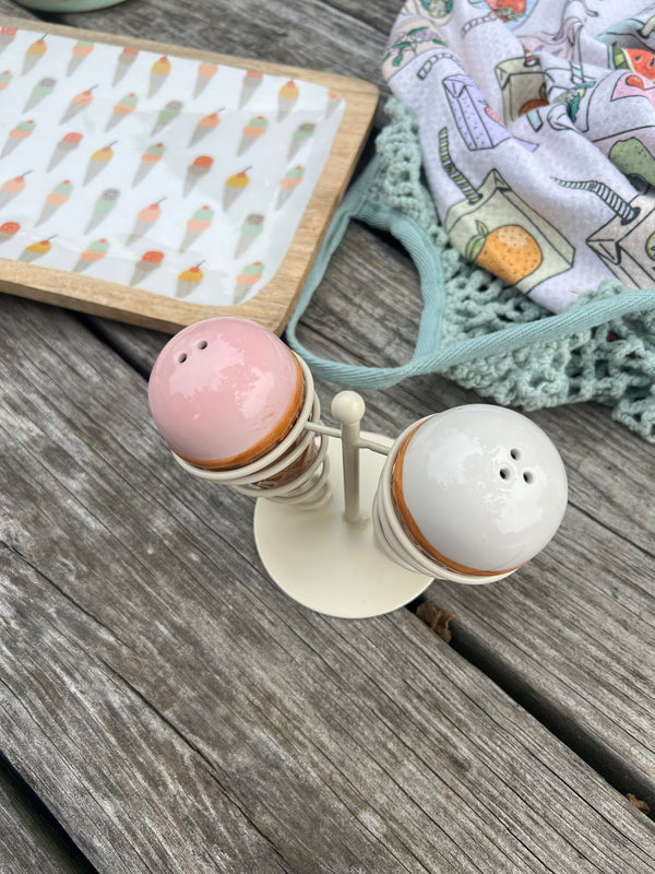 Salt and pepper shakers on a wooden surface with a patterned cloth in the background