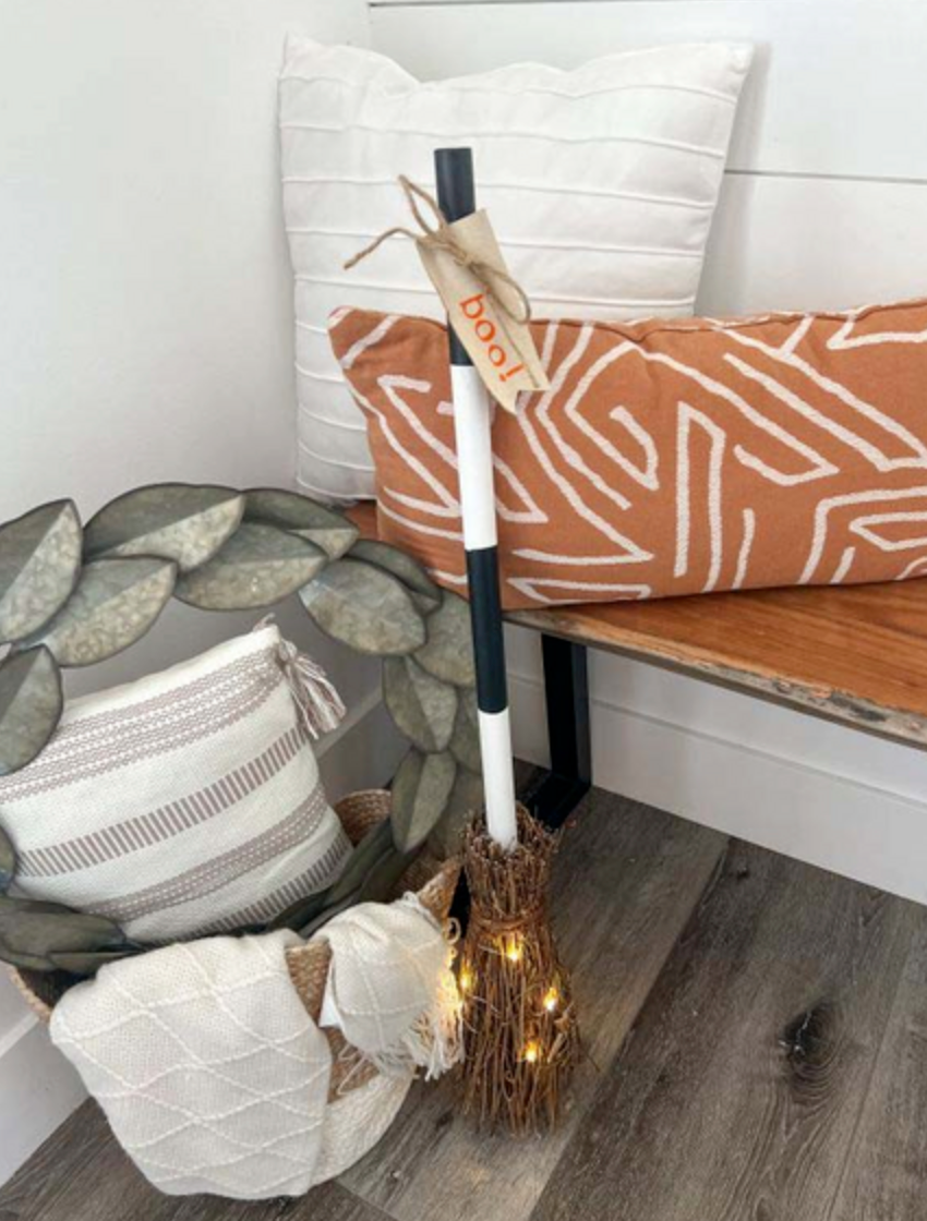 Decorative broom with lights leaning against a bench with patterned cushions.