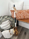 Decorative broom with lights leaning against a bench with patterned cushions.