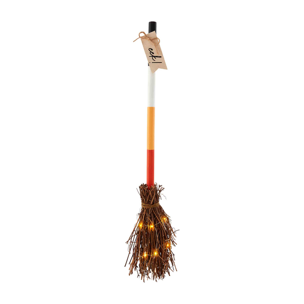 A broom designed to resemble a witch's broom with a white handle, orange shaft, and brown bristles, with a tag indicating it is for sale at a yard sale.