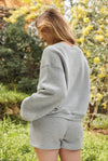Person wearing a gray sweatshirt and shorts set in a natural setting with trees and yellow flowers.