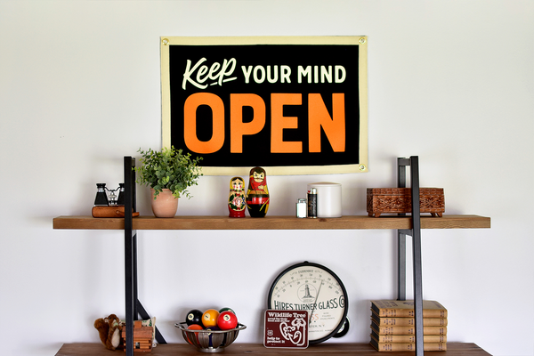 Decorative shelf with a 'Keep Your Mind Open' sign and various items on a white wall.