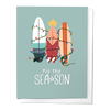 A greeting card with surfboards decorated in Christmas lights, titled 'TIS THE SEA-SON' on a blue background.