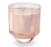 A multicolored striped glass candle, with a pinkish hue at the bottom, sitting inside a box with shiny, tinsel-like details.
