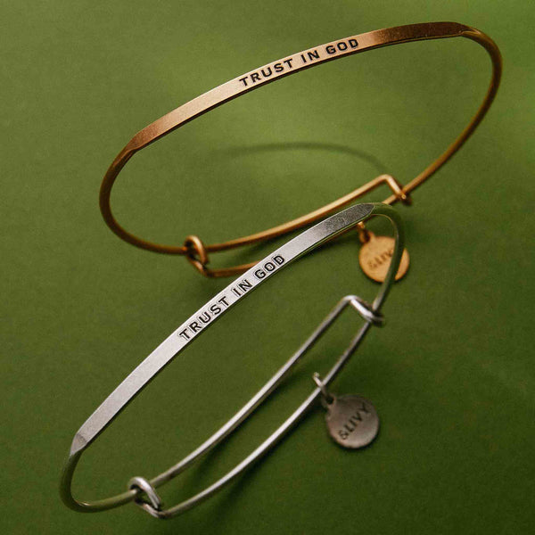 Two bangles, one gold and one silver, with 'Trust in God' engraving on a green background.