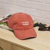 Red cap with 'I'm not for everyone' text on a wooden surface with a magazine and sunglasses.