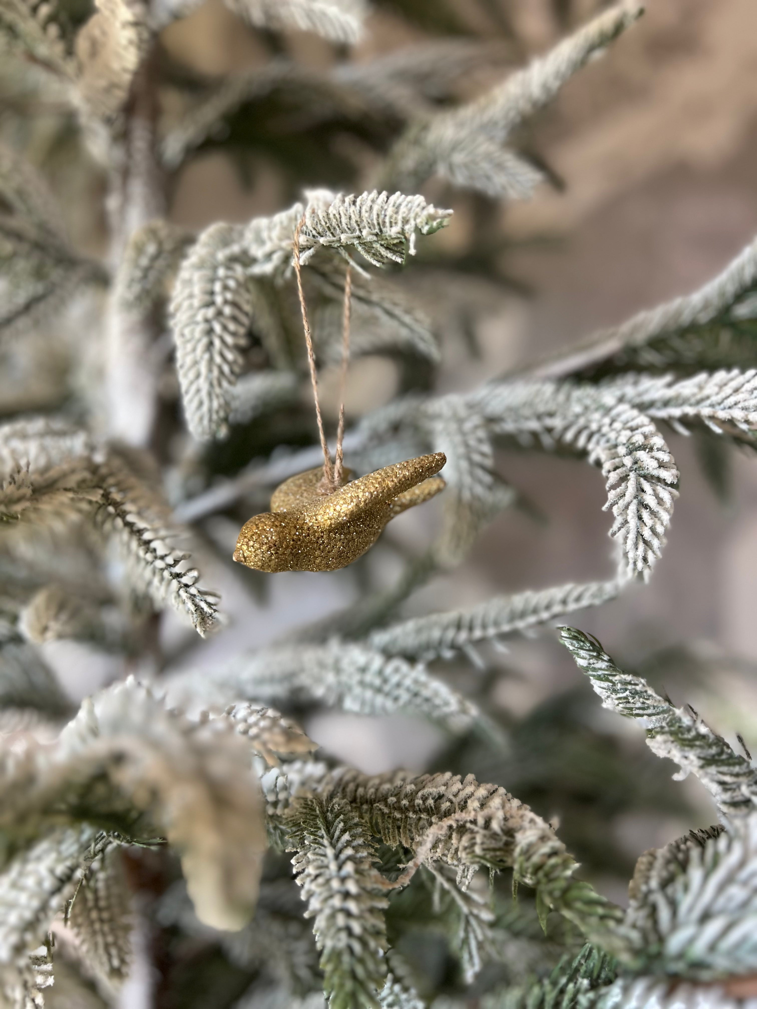 A gold-finished resin bird ornament hanging on a festive Christmas tree.