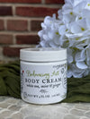 Jar of Balancing Act Body Cream with white flowers and green fabric in the background