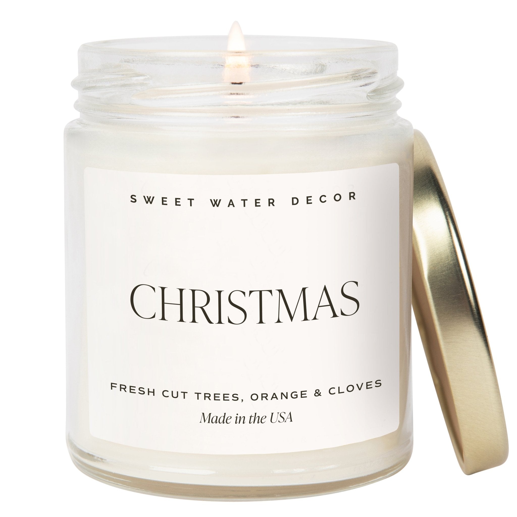 A clear jar soy candle with a label reading 'Christmas' for the festive season, indicating a fresh cut trees, orange & cloves scent, and being made in the USA.