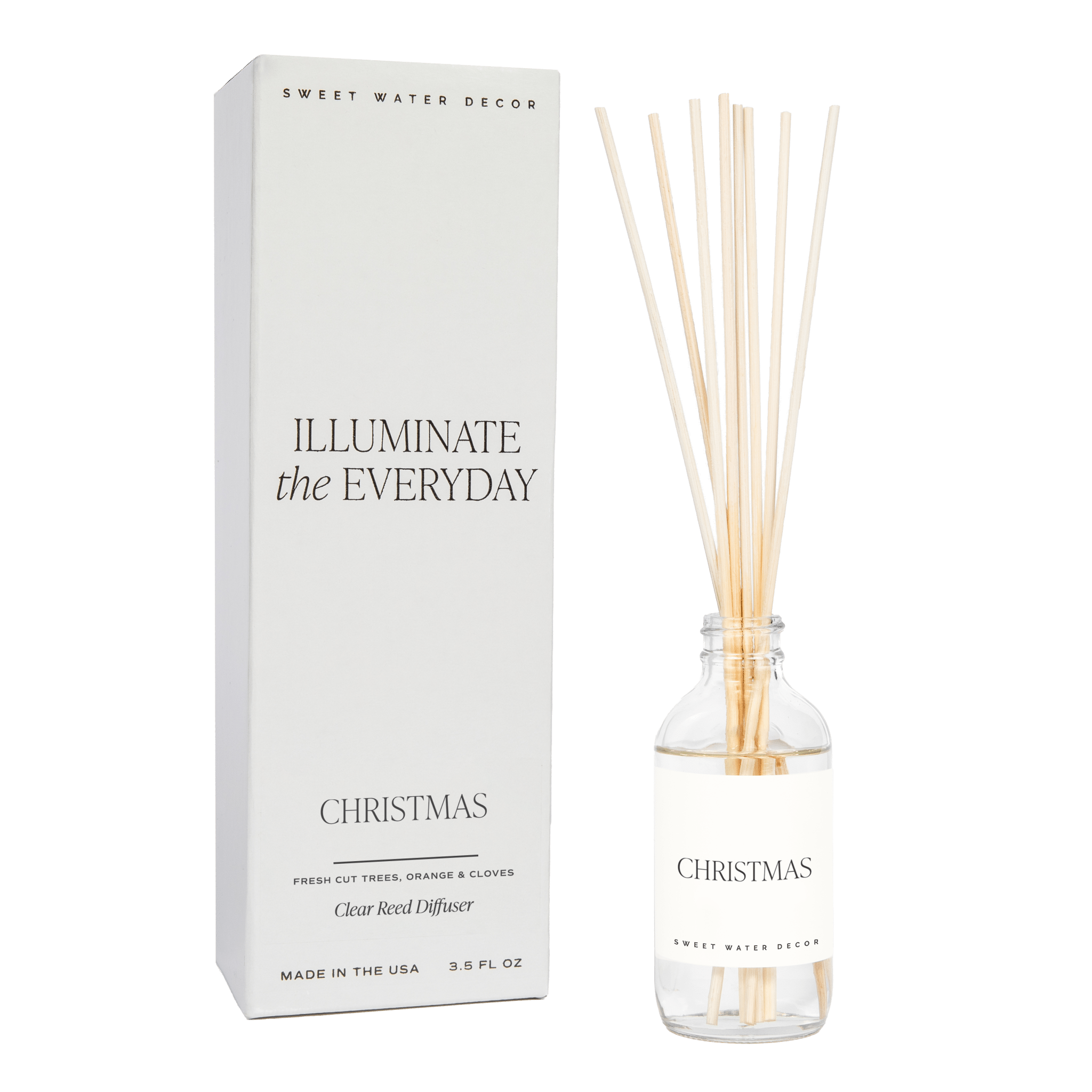A clear reed diffuser with Christmas-themed fragrance notes, including apple cider, cinnamon, fresh cut Christmas tree, cookies, orange peels, and cloves. The product packaging is also visible with the text 'Illuminate the Everyday' and 'Christmas'.