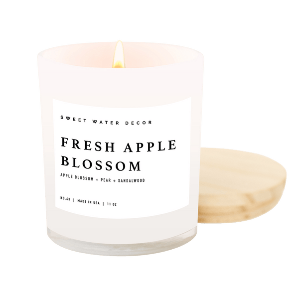 An 11 oz soy wax candle with a label reading 'Fresh Apple Blossom' from Sweet Water Decor, placed in a white jar with a cotton wick.