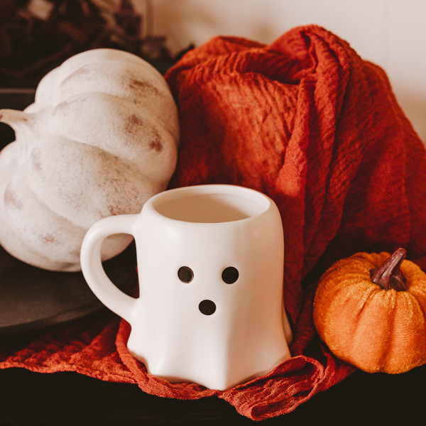 White mug with ghost design on a red blanket with pumpkins