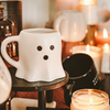 White ghost-shaped mug on a wooden stool with candles in the background