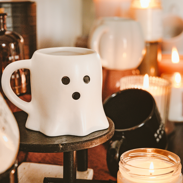 White ghost-shaped mug on a wooden stool with candles in the background