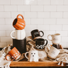 Collection of Halloween-themed mugs on a wooden tray with a tiled wall background.