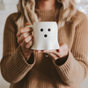 Person holding a white mug with black dots, wearing a brown sweater.
