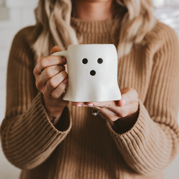 Person holding a white mug with black dots, wearing a brown sweater.