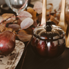Decorative black pot with a lid on a table with autumn leaves and a glass of red wine.