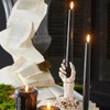 Decorative candle holder shaped like a hand holding a candle, with candles and books in the background.
