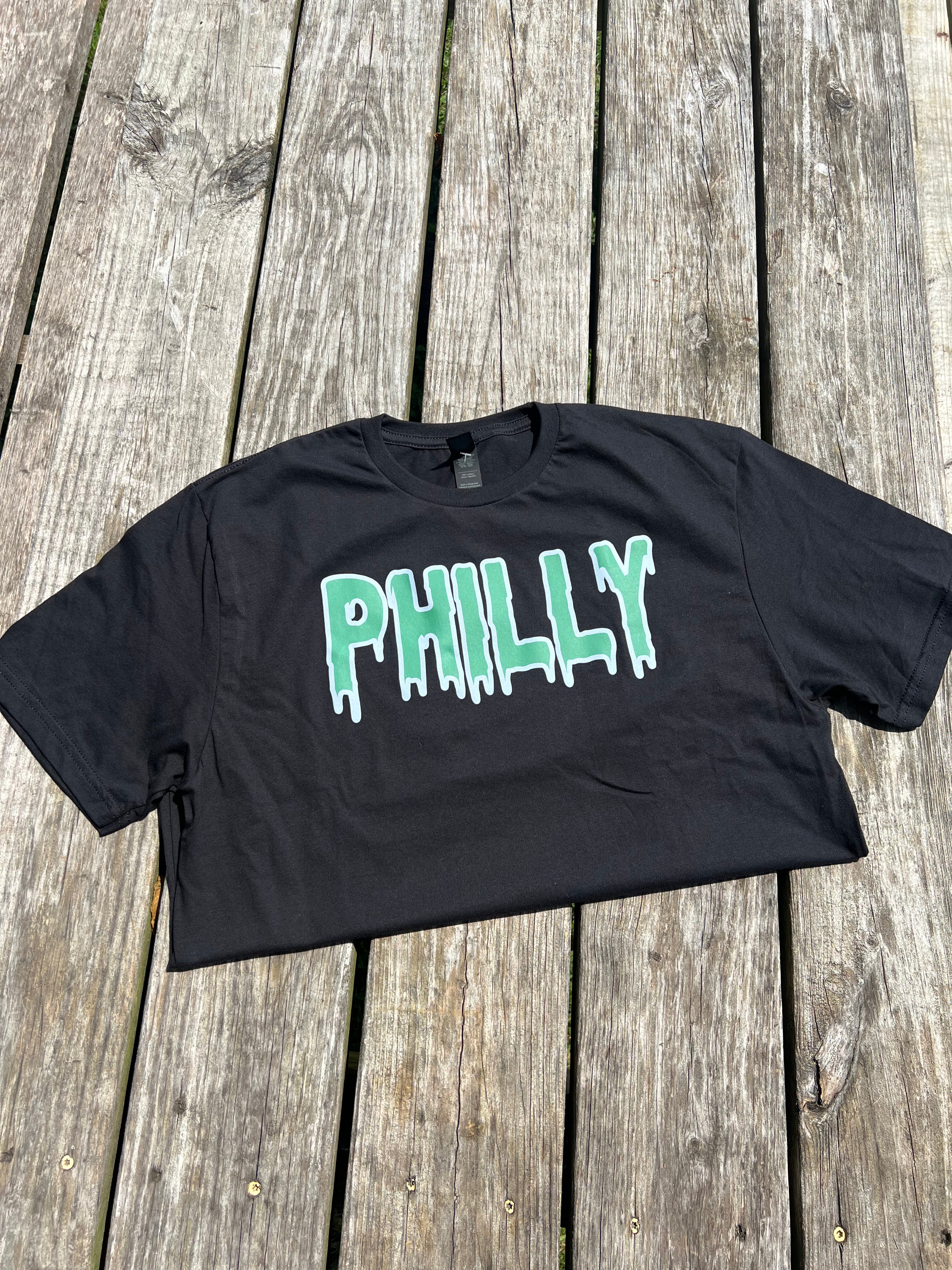 Black t-shirt with 'PHILLY' printed in green on a wooden surface