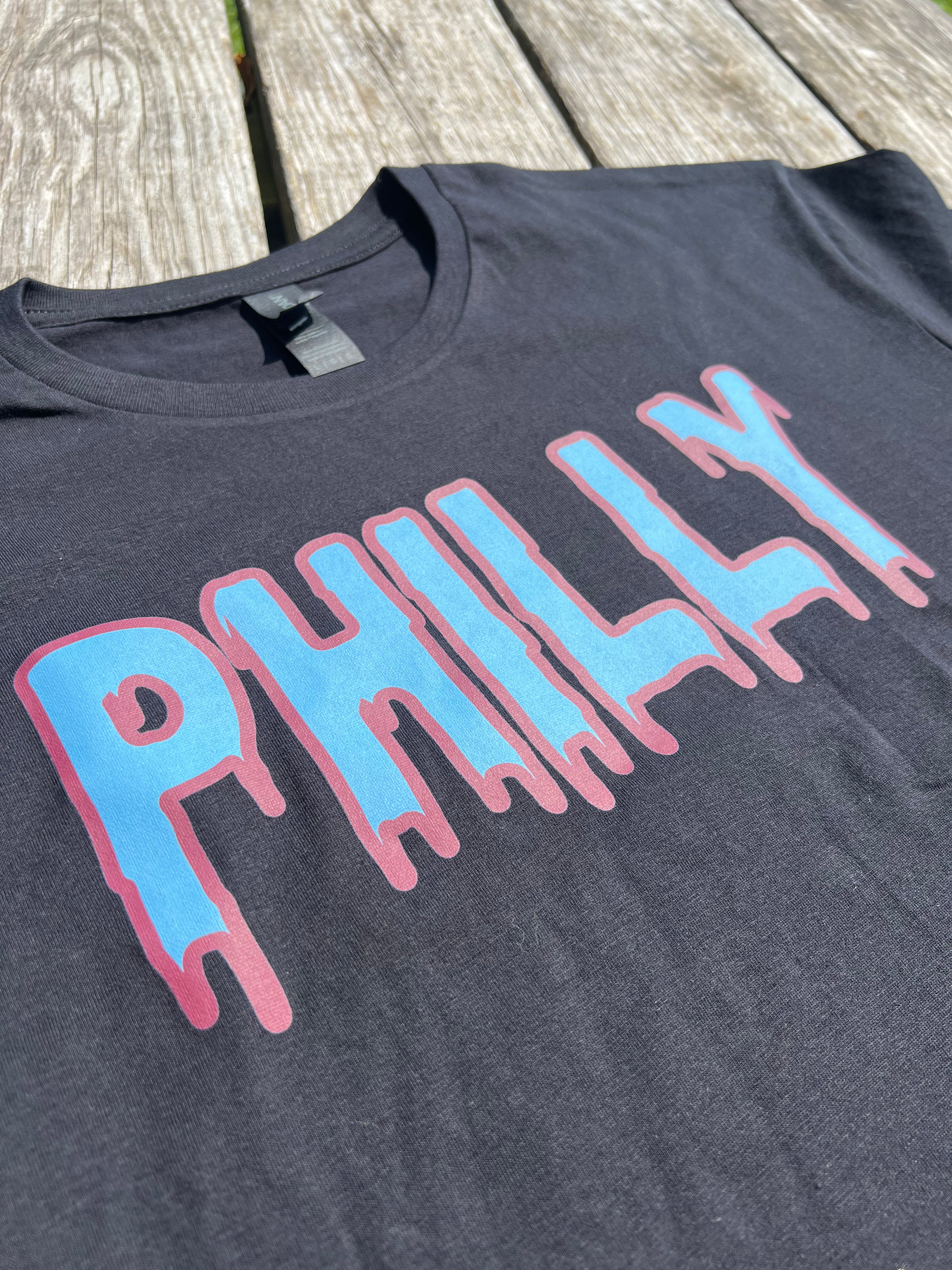 Black t-shirt with 'PHILLY' printed in blue and pink on a wooden surface