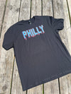 Black t-shirt with 'PHILLY' printed on it in pink and blue, laid flat on a wooden surface.