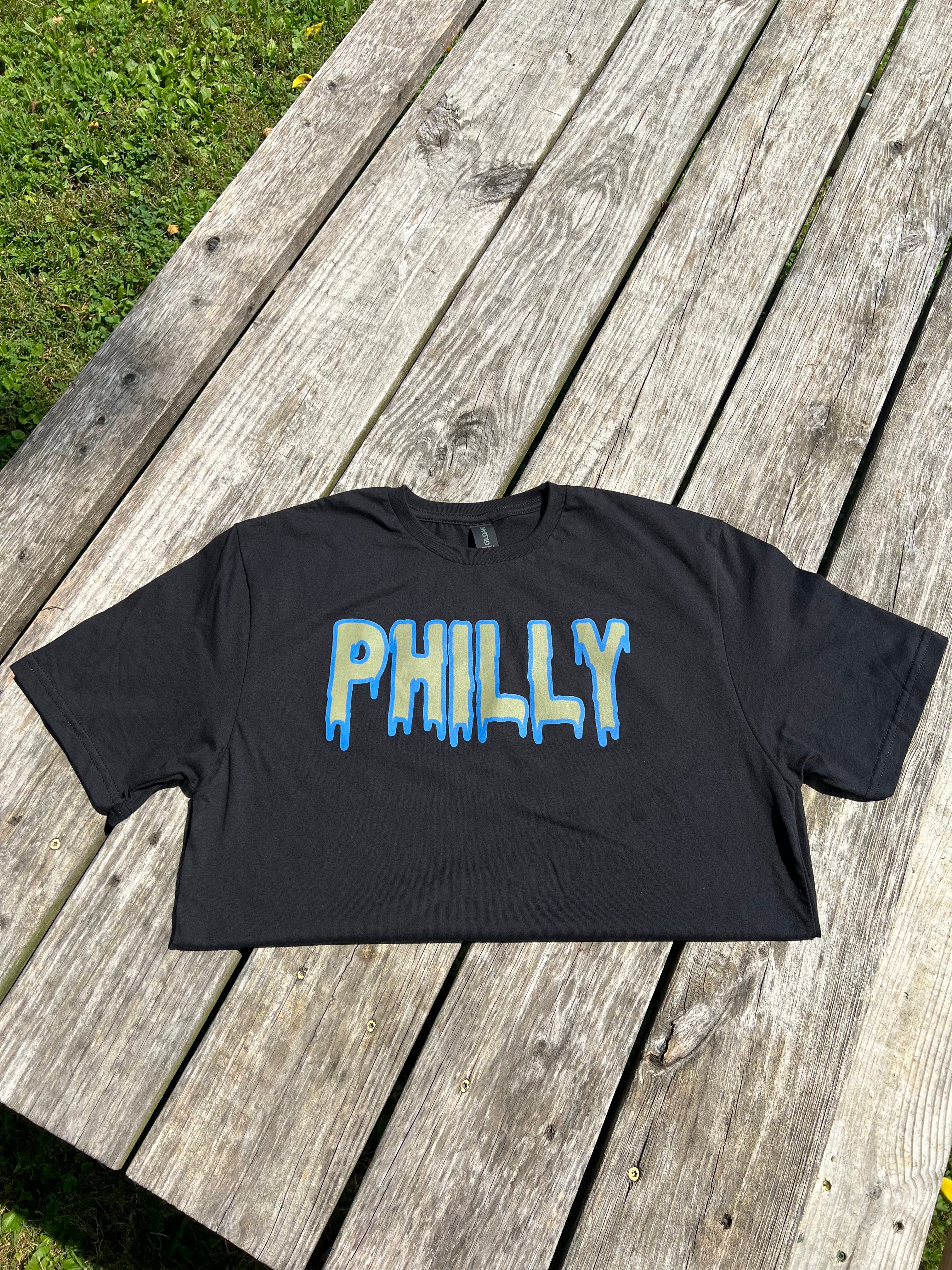 Black t-shirt with 'PHILLY' printed on it, placed on a wooden surface.