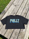 Black t-shirt with 'PHILLY' printed on it, placed on a wooden surface.