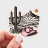 Sticker with a cactus, pink cowboy hat, and mountain landscape with 'Long Live Rad Women' text, held by a hand.