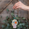 Hand holding a decorative hanging tag with floral design and text against a wooden background