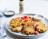 Fried chicken cutlets on a plate with tomatoes and a bottle of bacon sauce in the background.
