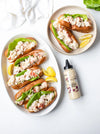 Plated seafood rolls with lemon wedges and a bottle of aioli on a white surface