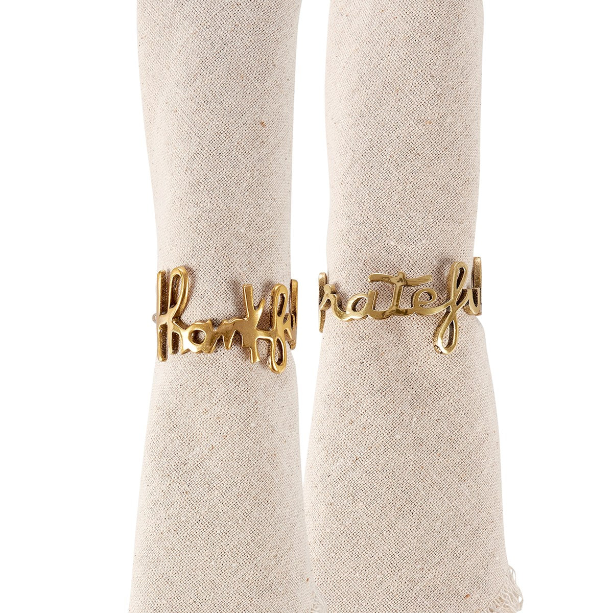 A set of two gold brass napkin rings with the word 'handful of love' written on them, displayed on a textured beige fabric.