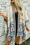 Woman wearing a patterned poncho with fringe against a brick wall.