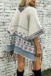 Person wearing a patterned poncho against a textured white brick wall.