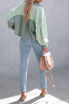 Person wearing a green jacket and light blue jeans with a pink handbag against a gray background