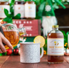 Hot toddy being poured into a mug with a bottle of Hot Toddy on a wooden table.