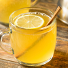 Glass mug with yellow liquid, lemon slice, and cinnamon stick on a wooden surface